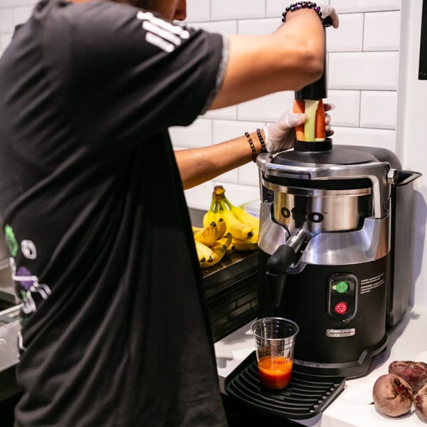 A Protini Bar employee juices carrots and celery, with bananas and beets nearby.