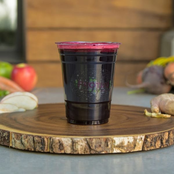 A Protini Bar beet juice with foam on a wooden slab, surrounded by fresh produce.