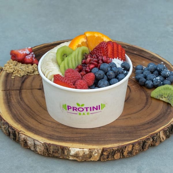 A Protini Bar acai bowl overflowing with fresh fruit, including kiwi, oranges, strawberries, and blueberries.